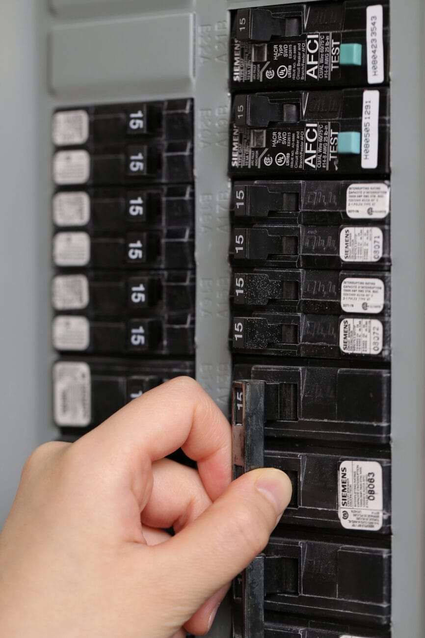 A hand is flipping a switch in an electrical circuit breaker panel.